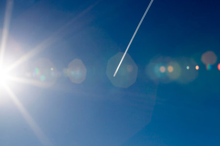 traces of flying aircraft and beautiful blue sky and sunlight with white bright clouds illuminated...