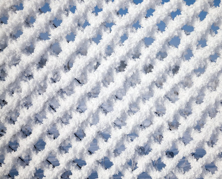 mesh netting galvanized covered with white pieces of snow and frost, close-up of the fence in the...