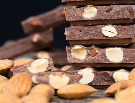 delicious roasted almonds and large pieces of chocolate on a wooden table, close-up of natural cocoa products with added sugarの写真素材