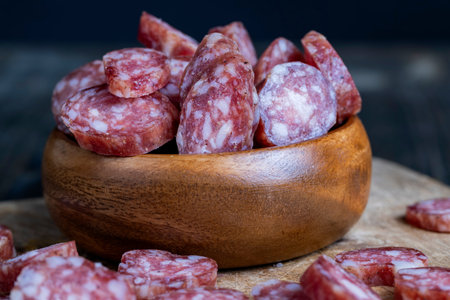 sliced thin sausage with bacon on a wooden dish, sliced pork sausage and other ingredients on the...