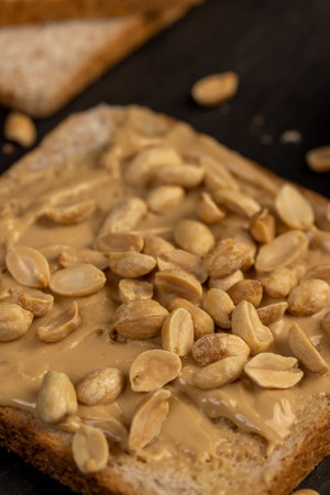 wheat bread with bran and soft peanut butter, peanut butter on a piece of bread and roasted peanuts on the table, close upの写真素材