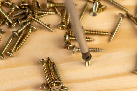 screwdriver and screws on a wood board, golden colored screws for construction, board and metal...