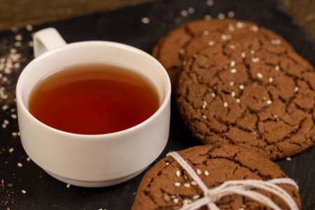 biscuits with white sesame and cocoa, sweet chocolate-flavored biscuits with sesame seeds on the table, close up, a cup of tea next to a cookieの写真素材