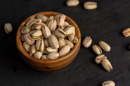 roasted pistachio nuts in their shells with added salt, roasted unpeeled pistachio nuts in a wooden bowl with cracked shells, close upの写真素材