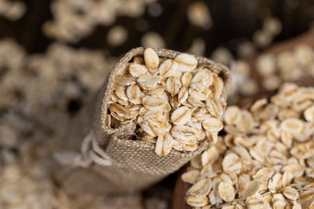 one linen bag with oatmeal flakes for making porridge, scattered dry cereal flakes from oats, flattened, steamed and dried, closeupの写真素材