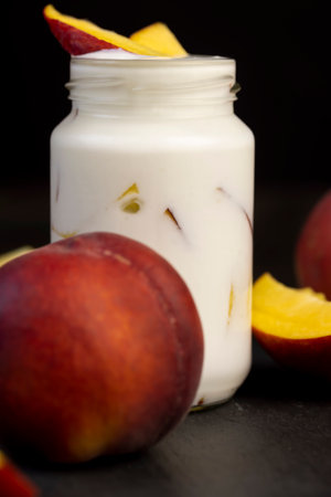 yogurt and ripe peaches cut into pieces on black slate, fermented milk product with peach flavor with the addition of pieces of ripe peach, closeupの写真素材