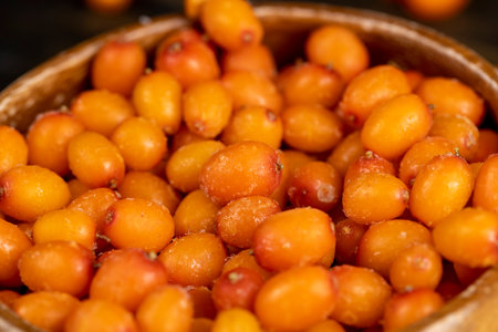 frozen orange sea buckthorn berries in a wooden bowl on the table, defrosting ripe sea buckthorn berries to make a drinkの写真素材