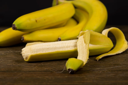 greenish open ripe bananas on the table, a bunch of bananas on a blackboard one of which is open, close-upの写真素材