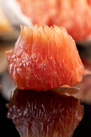 red citrus on the black mirror, peeled citrus grapefruit with red flesh, the fruit is reflected on a black mirror surface, close up, side viewの写真素材