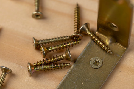 one yellow corner with holes for connecting wooden parts with screws, metal building products for connecting wooden structures, scattered screws on a pine board, side viewの写真素材
