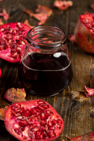 sliced red pomegranate on a black table and a jar of pomegranate juice , red pomegranate cut into pieces next to natural pomegranate juiceの写真素材