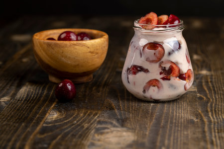 fresh cow cream yogurt with cherry flavor and berry slices, glass jar with cherry yogurt with fresh red cherries closeupの写真素材