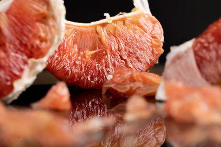 citrus on the black mirror, peeled citrus grapefruit with red flesh, the fruit is reflected on a black surfaceの写真素材
