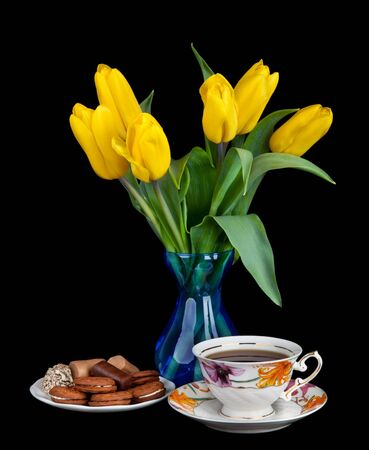 Bouquet of yellow tulips in glass vase and Antique tea cup full of tea on black backgroundの写真素材