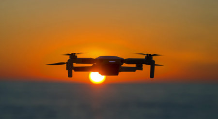 Drone flying in the sky against the backdrop of a bright sunset. Radio-controlled quadcopter with a...