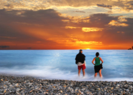 A man and woman in bokeh looking at at sunset, standing in the waves (background concept)の写真素材