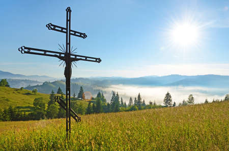 Cross-crucifixion in the field on a sunny day with fog in the mountains (pilgrimage, harmony, inspiration, peace - concept)の写真素材