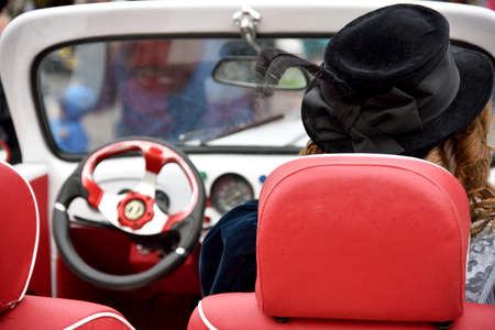 Curly girl in medieval dress and hat with feathers in retro car.の写真素材