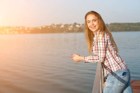 Beautiful young girl resting on a pier near the water at dawnの写真素材
