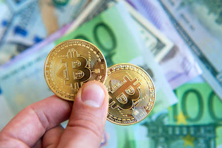 two bitcoins in their hands over dollar and euro bills (Investment, exchange rate, rise, decline, luxury, success, stock exchange - concept)の写真素材
