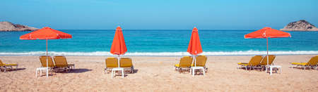 Abstract image with sun loungers and orange umbrellas from the sun on the beach on the seafront with waves (relaxation, harmony, holidays - concept)の写真素材