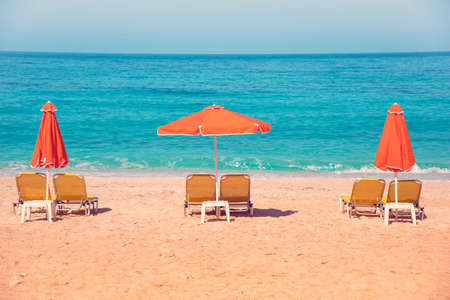 Abstract image with sun loungers and orange umbrellas from the sun on the beach on the seafront with waves (relaxation, harmony, holidays - concept)の写真素材