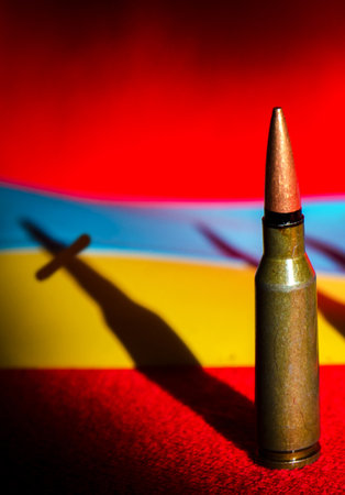 Abstract image with a bullet from a machine gun and a shadow in the form of a grave cross on the background of the flag of Ukraine. (War in Ukraine - concept)の写真素材