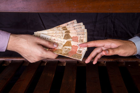 First person is giving 5000 Rupees Pakistani Currency Notes to another Person under the table .
