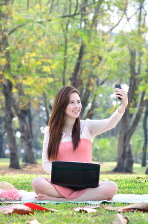 woman sitting on wooden mat and take a photo at park.の写真素材
