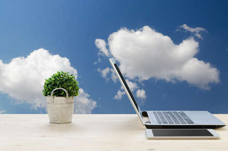 Office Desk with Notebook, tablet , small tree on basket and Blue sky Background. Business concept background.の写真素材