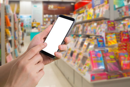 human hand hold and touch blank screen smart phone, tablet, cellphone on blurry bookshelf in...
