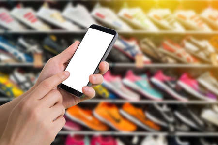 human hand hold and touch smartphone, tablet, cell phone with blank screen on blurry shelf of shoes, concept of shopping online.の写真素材