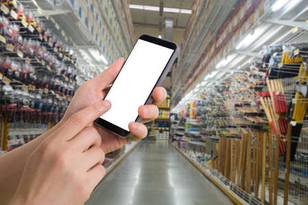 human hand hold smartphone, tablet, cell phone with blurry hardware store. concept of shopping and finding hardware tool for house repair.の写真素材