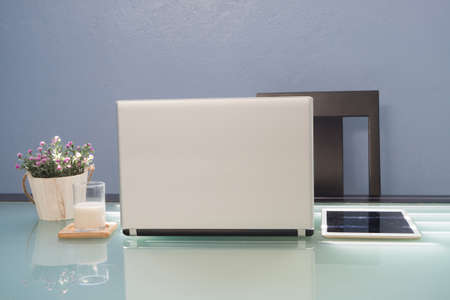 Office table with laptop, tablet, pink rose flower on pot and glasses of water. Concept of work place at home.の写真素材