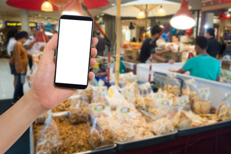 human hand hold and touch smartphone, tablet, cell phone with blank screen on blurry street food...
