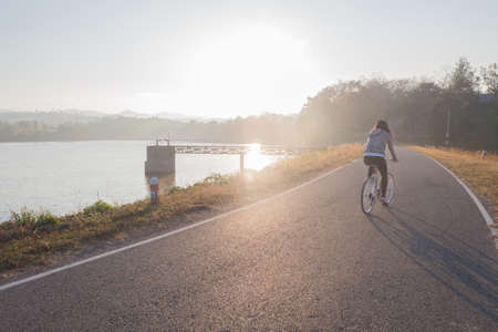 young woman ride bicycle on load dam in morning, concept of Asian people healthy lifestyle.の写真素材