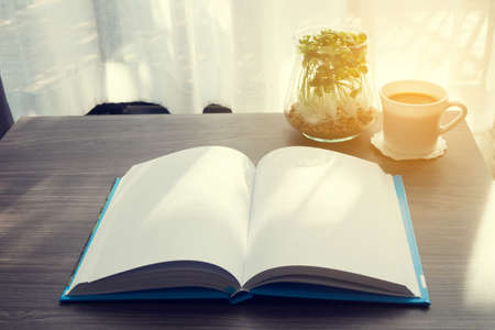 office table with blank screen on notebook paper, morning coffee and garden plant on flowerpot,  concept of holiday relaxing, vintage effect style.の写真素材