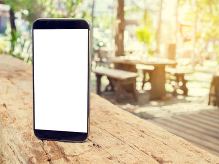 wood table with blank screen smartphone, tablet, cell phone ob blurry tree garden background.の写真素材