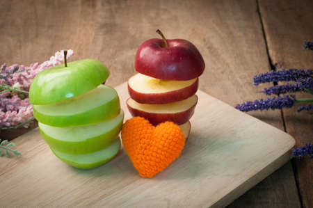 kitchen table with orange heart shape, stack of slice  green and red apple  on cutting board-healthy eating and dieting food, concept of health care lifestyle.の写真素材
