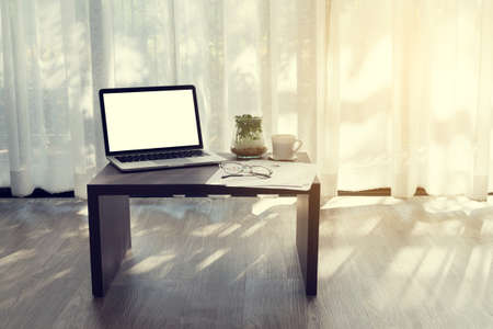 Office desk with  blank screen on laptop, cup of coffee ,modern eyeglasses, sale online report statistic paper, garden tree on pot and windows curtains background. concept of business lifestyle.の写真素材