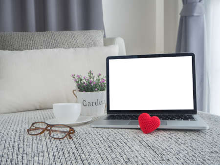 bed with blank screen for text on laptop, white ceramic white coffee cup, modern eyeglasses, pink rose on pot  and red heart shape sing at bedroom.の写真素材