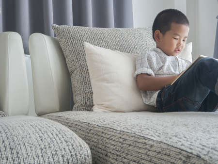 Asian children using tablet on modern vintage sofa at living room. concept of southeast Asia children with learning technology at home.の写真素材