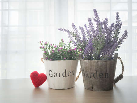 wood table with beautiful pink rose  flower, purple lavender flower and red heart shape sign on beautiful white drape window texture background at living  room.の写真素材