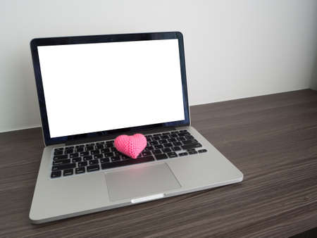 wood table with blank screen on laptop and pink heat shape sign on keyboard. view form front office table.の写真素材