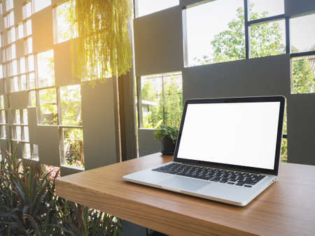 wood table with blank screen on laptop computer on natural tree garden.の写真素材