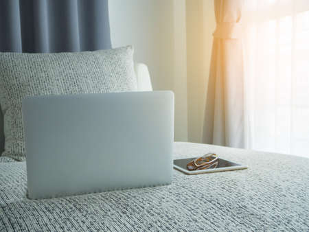 modern vintage sofa with back screen  laptop and  eyeglasses on tablet on blurry beautiful white drape window texture background at bedroom.の写真素材