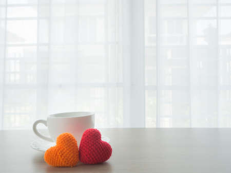 kitchen table with white ceramic coffee cup, red and orange heart shape sign on blurry beautiful white drape window texture background. concept of healthy care.の写真素材