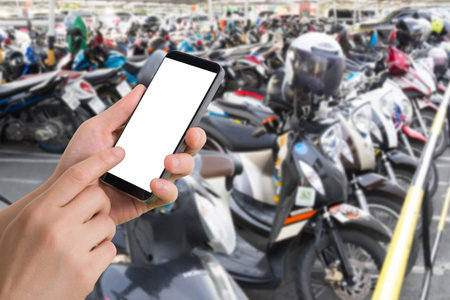 human hand hold smartphone, tablet, cell phone on blurry parking motorcycle. concept of trace...