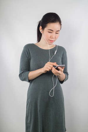 young woman be pregnant in maternity clothes listening to music on cement wall background.の写真素材