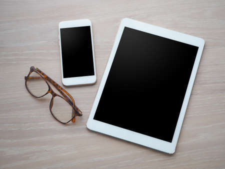 wood office table with blank screen for text on tablet, smart phone, cell phone and modern eyeglasses. view from top wood table.の写真素材